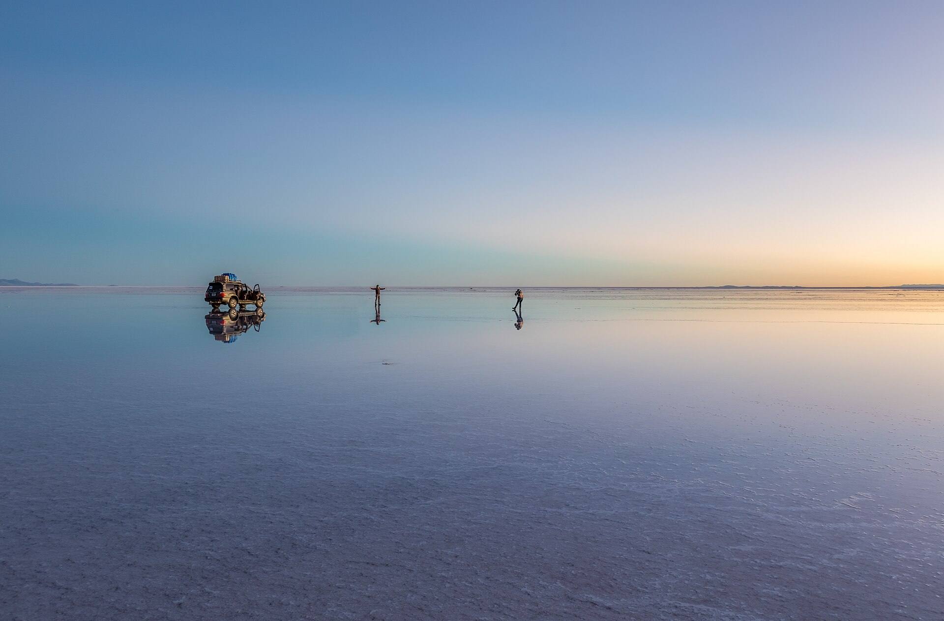 Travellers and a vehicle reflected at sunrise on the Salar de Uyuni.