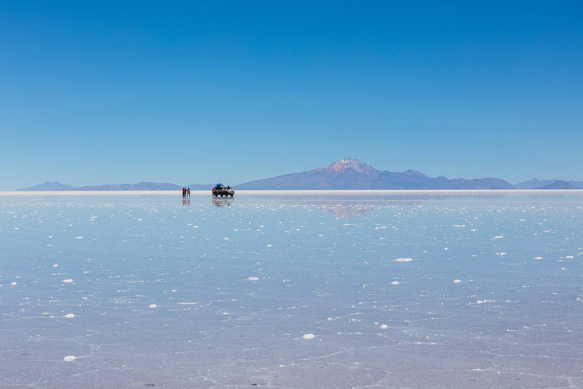 Horizonte branco e veículo distante no Salar de Uyuni.